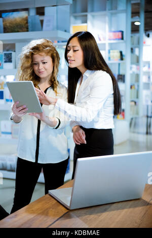 two female coworkers discussing with each other using laptop on table in design studio Stock Photo