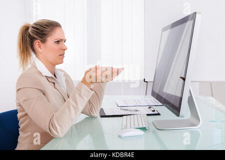 Businesswoman Looking At Computer Gesturing At Workplace Stock Photo