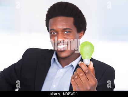 Happy Young Businessman Holding Light Bulb With Green Grass Stock Photo