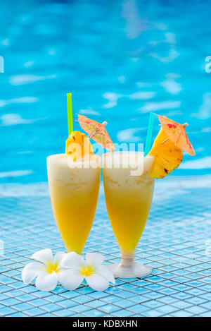 two glasses of cocktail beautifully decorated with pineapple and flowers on the edge of the pool Stock Photo