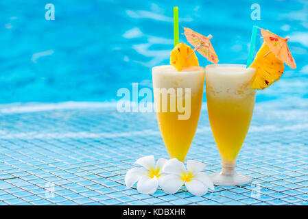 pineapple cocktail beautifully decorated with umbrellas and flowers on the edge of the pooll Stock Photo