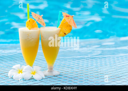 delicious pineapple cocktail beautifully decorated with umbrellas and flowers on the edge of the pool Stock Photo
