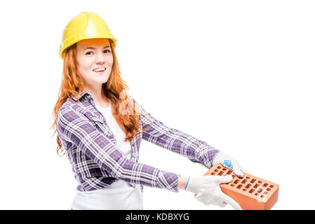 beautiful woman with red hair holds a brick, wearing a yellow helmet on her head Stock Photo