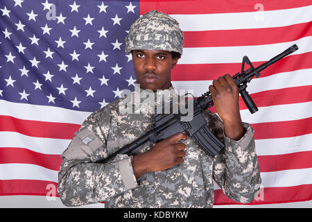 African American Soldier Standing With Gun Standing In Front Of Us Flag Stock Photo