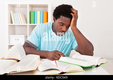 Worried Young African Man Studying At Home With A Lot Of Books Stock Photo