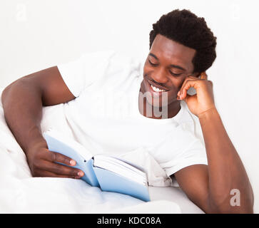 Happy Young African Man  Reading His Book On Bed Stock Photo