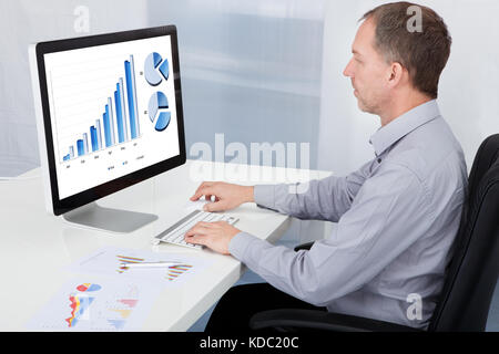 Mature Businessman Analyzing Graph On Computer At Office Stock Photo