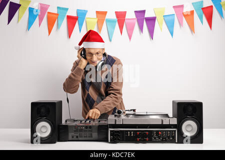 Old DJ with a christmas hat playing music against a wall with decoration flags Stock Photo