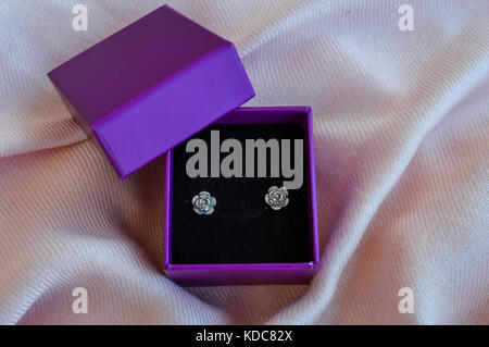 Silver earrings in a purple box, isolated on pink fabric background Stock Photo