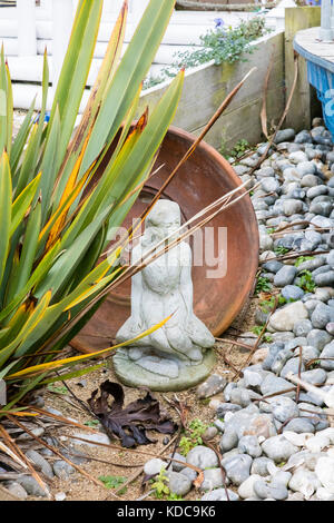 A small statue and a flower pot amongst pebbles and iris leaves in a front garden on Gillingham Strand, Kent, UK Stock Photo