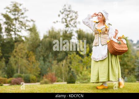Young beautiful peasant woman with a bouquet of sunflowers in purse or basket looks far away against the background of greenery Stock Photo