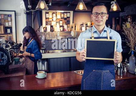 Portrait of smiling asian barista holding blank chalkboard menu in coffee shop. Cafe restaurant service, Small business owner, food and drink industry Stock Photo