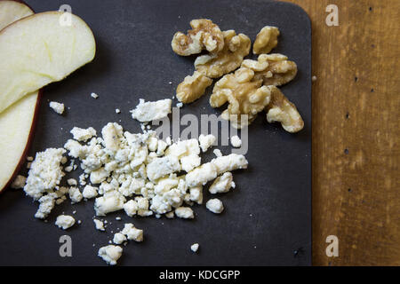 Close up of blue cheese crumbles with slices apple pieces and walnuts on black cutting board. Stock Photo