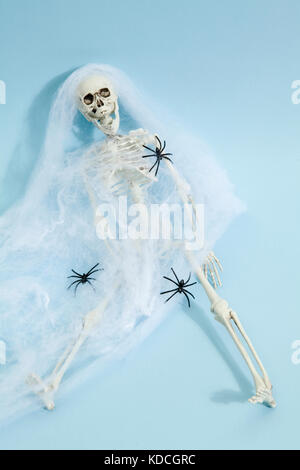 Plastic toy skeleton captured by a spider web on a vibrant pop blue background. Minimal color still life photography Stock Photo