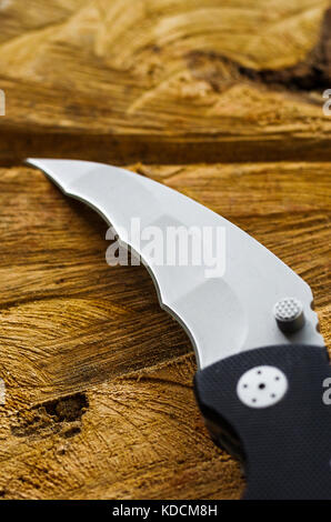 Knife blade in the form of a fang. Natural background of wood. Stock Photo