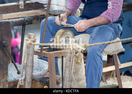 Asti, Italy - September 10, 2017: blacksmith sharpens the hatchet with an abrasive stone Stock Photo