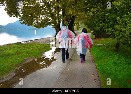 A couple in fold-up raincoats walk beside Lake Bled in Bled, Slovenia. Stock Photo
