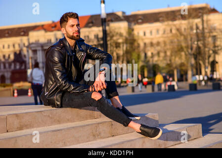 A handsome young hipster man sitting and relaxing on the stairs on a square Stock Photo