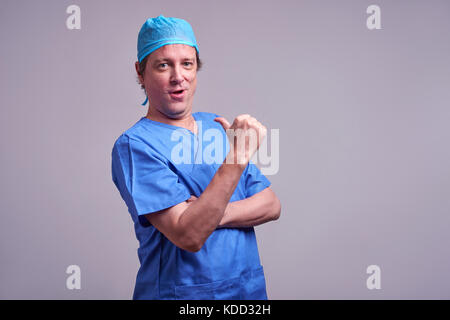 A middle aged male doctor standing confidently in a blue scrubs and pointing to himself Stock Photo