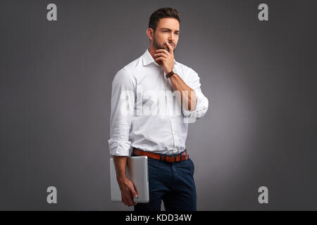 A handsome young man thinking and holding a laptop in a white shirt Stock Photo
