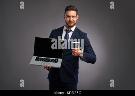 An elegant handsome young man holding and showing the screen of a laptop while showing thumbs up Stock Photo