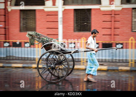 Manual Rickshaw wala on the wet streets of Kolkata in India. One of the few places to see this occupation. Running man pulling rickshaw on street Stock Photo