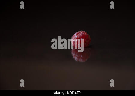 Close up of a raspberry resting on a black surface upside down. Stock Photo