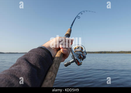 Fishing on a lake. Fishing rod with a reel in hand.clear  blue sky. Stock Photo