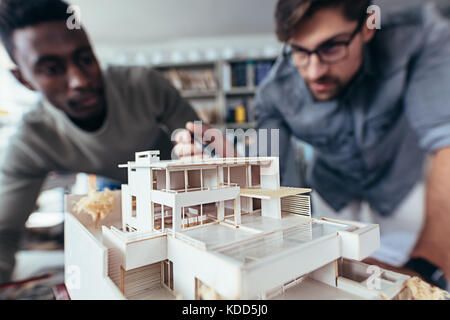 Close up shot of scale model house on table with architects. Two architects making architectural model in office together. Stock Photo