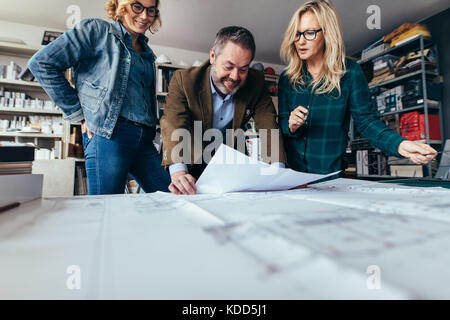 Designers finalize a housing construction plan in office. Architects looking at building blueprints. Stock Photo