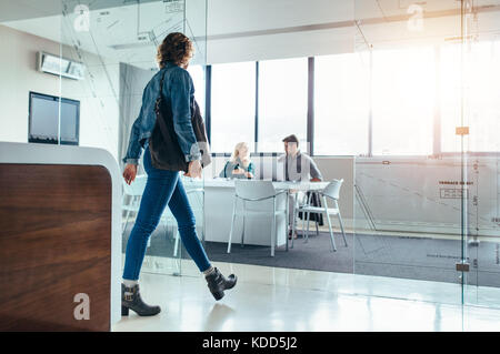 Female client moving forward towards conference room for meeting with designers. Creative office with executives in meeting hall and client outside. Stock Photo