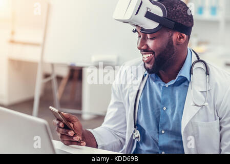 Relaxed African American doctor in virtual reality glasses using smartphone Stock Photo