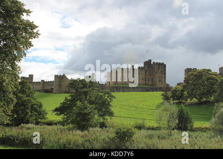 Alnwick Castle under late summer storm clouds viewed from the north looking south over the River Aln across parkland, Alnwick, Northumberland, UK Stock Photo