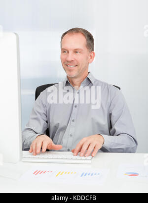 Portrait Of Mature Businessman Using Computer At Desk Stock Photo