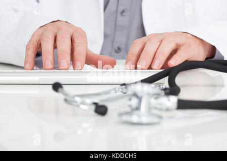 Close-up Of Doctor's Hand Typing On Keyboard In Front Of Stethoscope Stock Photo