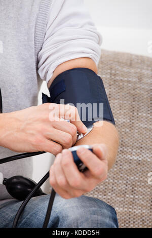 Man Sitting On Couch Checking His Own Blood Pressure Stock Photo