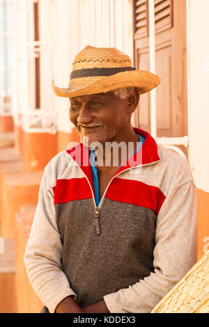 Smiling local Cuban man with hat sitting outside a house watching the day go by near Plaza Major, Trinidad, Cuba, Caribbean Stock Photo