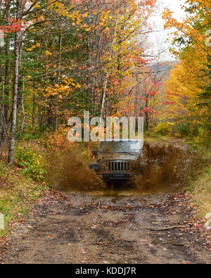 A Jeep Wrangler Rubicon charging through a water and mud hole in the Adirondack wilderness in autumn. Stock Photo