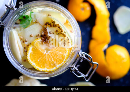 A colorful jar of homemade pickles with orange, coriander seeds, fresh ginger in contrast with dark tone black ground Stock Photo