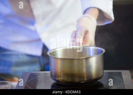 Cook's hands in white gloves hold a saucepan over an electric stove. Shooting with selective focus. Stock Photo