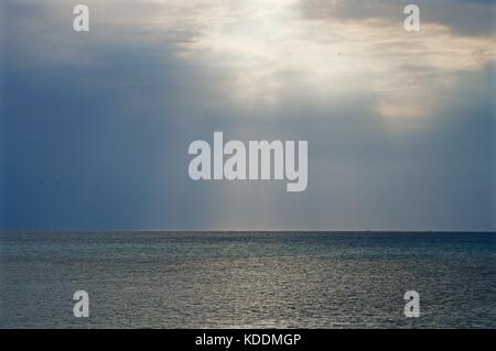 Sun breaking through clouds over ocean Stock Photo