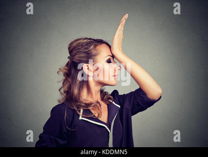 Regrets wrong doing. Sad woman, slapping hand on head having duh moment isolated on gray background. Negative human emotion feeling, body language Stock Photo