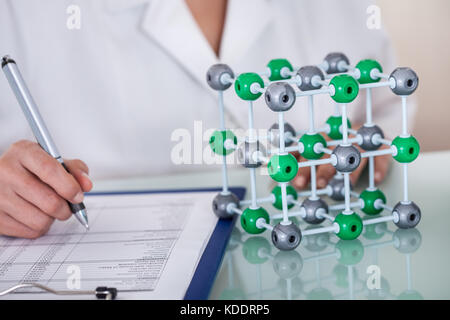 Female Scientist Sitting In Laboratory And Writing On Clipboard Stock Photo