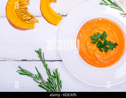 creamy pumpkin soup in a round white plate and pieces of fresh pumpkin on a white table, top view Stock Photo
