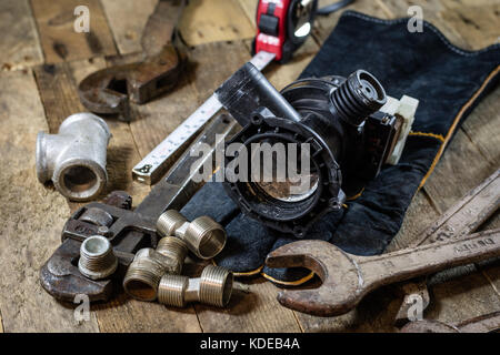 Hydraulics, tools for plumber on wooden table. Workshop, table and tools - adjustable spanner, connectors, keys. Black background Stock Photo