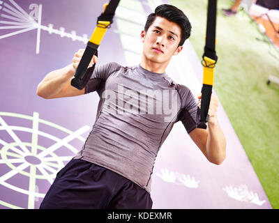 young asian man exercising in gym using fitness straps. Stock Photo