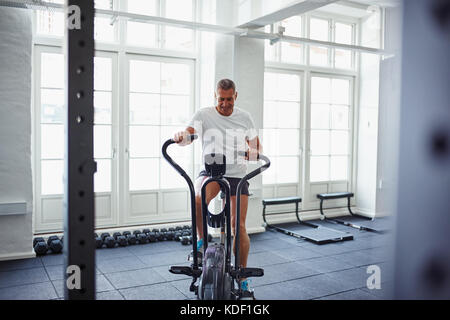 Determined mature man in sportswear pushing himself on a stationary bike while working out alone at the gym Stock Photo