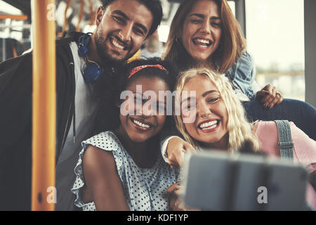 Diverse group of smiling young friends taking selfies while riding together on a bus Stock Photo
