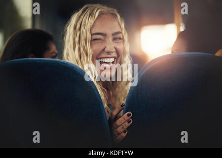 Laughing young blonde woman sitting alone on a bus looking over her shoulder and winking Stock Photo