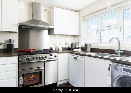 A small, clean, fresh, white kitchen with stainless steel range cooker, back splash & hood in a typical modern UK home. Stock Photo